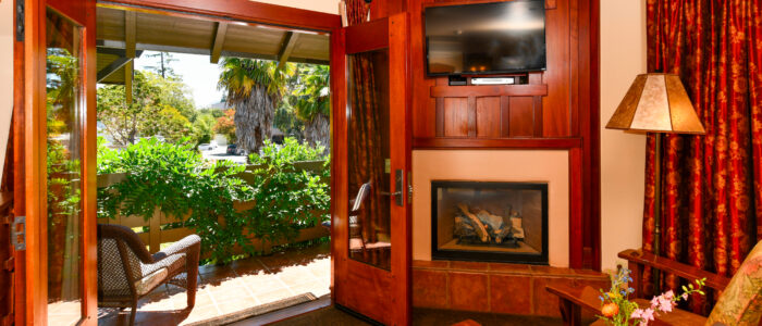 Room 4 Sitting Area 2 Chairs with Table in Between in Front of Fireplace. French Doors Open to Balcony with 2 Chairs and Table. Wisteria growing on Railings with Palms in Background