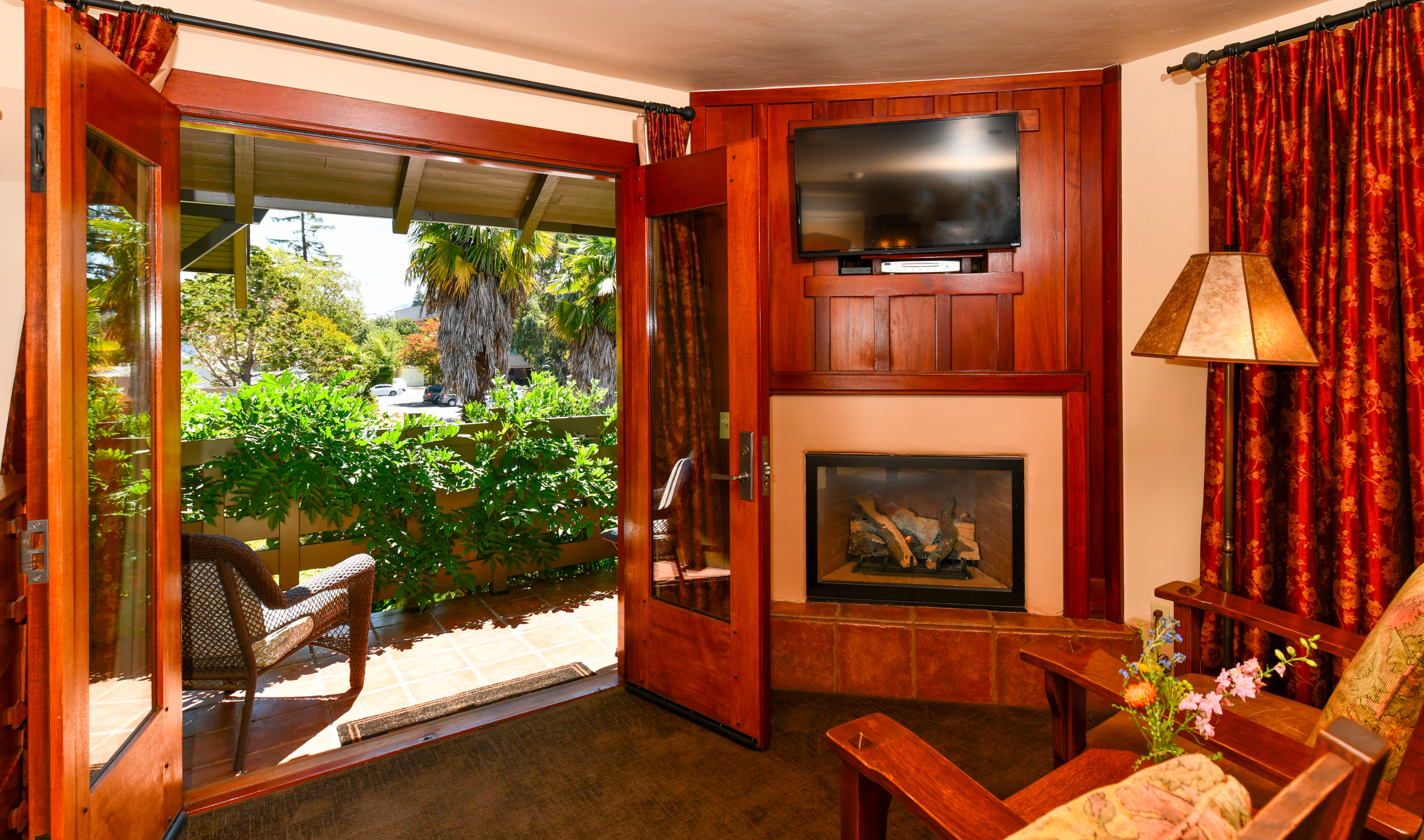 Room 4 Sitting Area 2 Chairs with Table in Between in Front of Fireplace. French Doors Open to Balcony with 2 Chairs and Table. Wisteria growing on Railings with Palms in Background