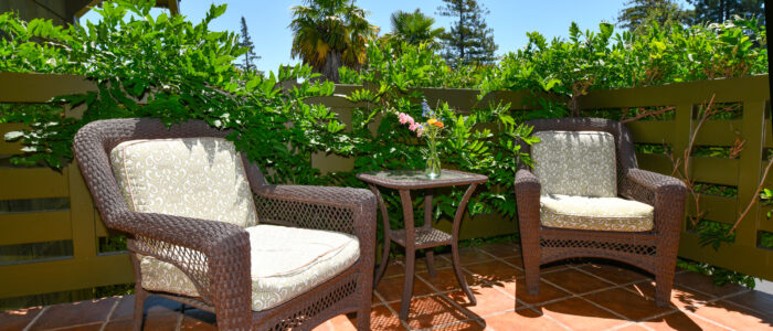 Room 4 Balcony with 2 Chairs and Table in Between. Flower on Table, Wisteria on Railings, Palms in Background