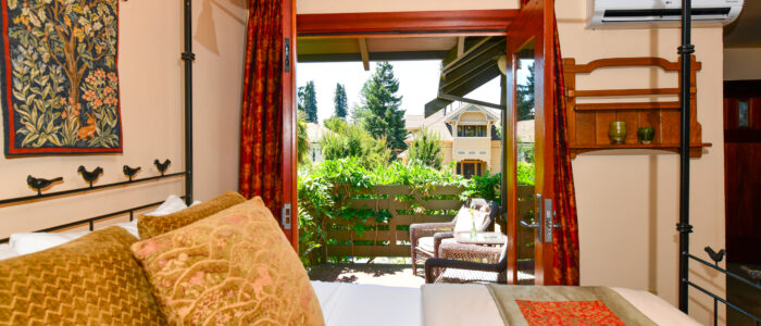 Room 8 King Bed, French Doors to Balcony with 2 Chairs and Table, Wisteria Vines, Trees in Background