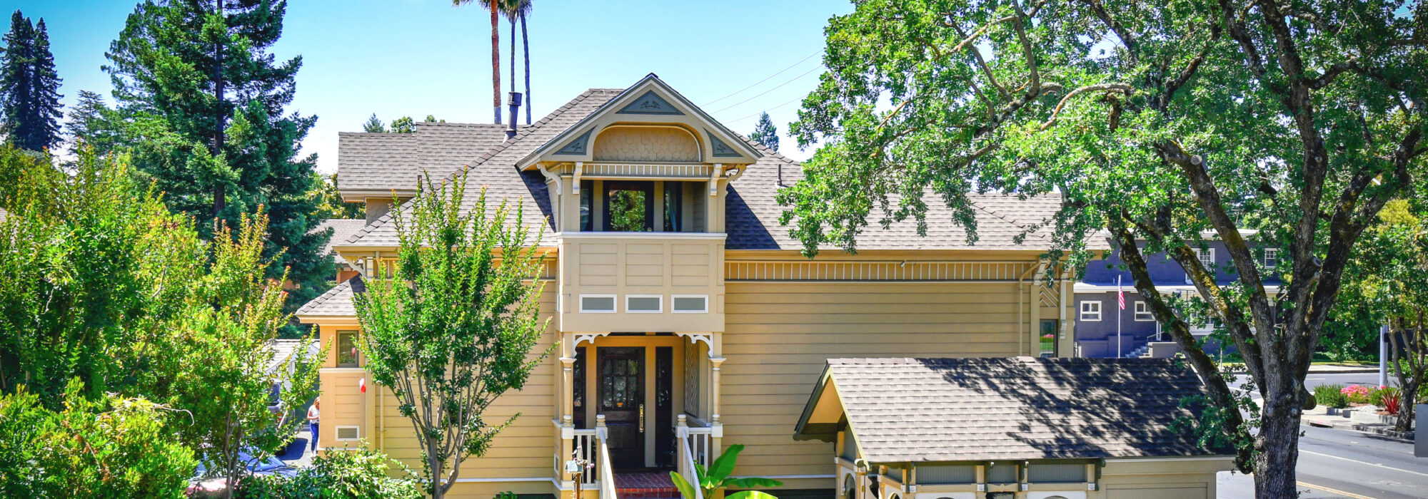 Eastlake, Queen Anne Styled Finch Guest House. Steep Red brick staircase leads to entry porch. Above Entry porch, a 2nd story cover porch mimics form of classic Victorian tower. Smaller building to right is gazebo. Landscaping is large valley oak and topicals near building.